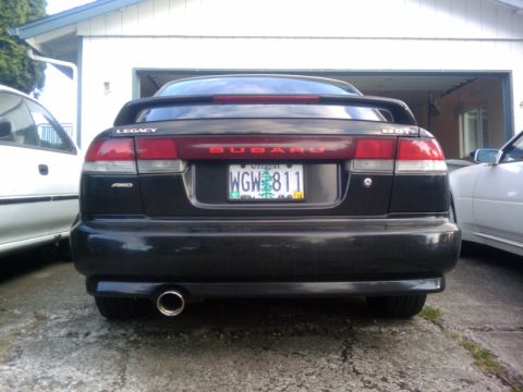 1998 Subaru Legacy - The rear of a black 1998 Subaru Legacy sedan is visible, parked next to another vehicle.