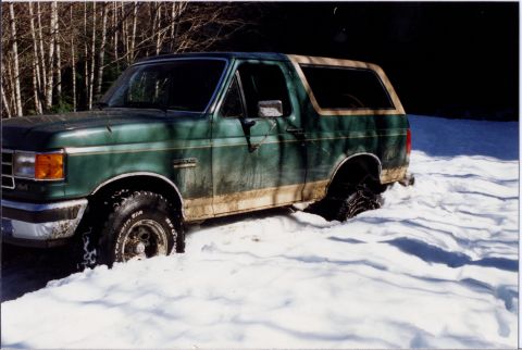 1990 Ford Bronco - A green 1990 Ford Bronco is stuck in deep snow, with only the top of the tires visible.