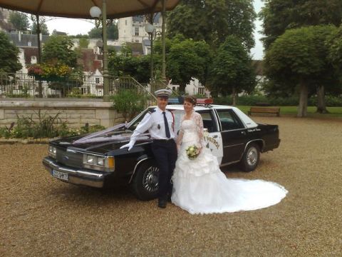 1991 Ford Crown Victoria - A police officer and a bride pose in front of a police car decorated with wedding ribbons.