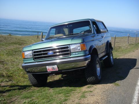 1990 Ford Bronco - 1990 Ford Bronco parked on a coastal road with the ocean in the background.