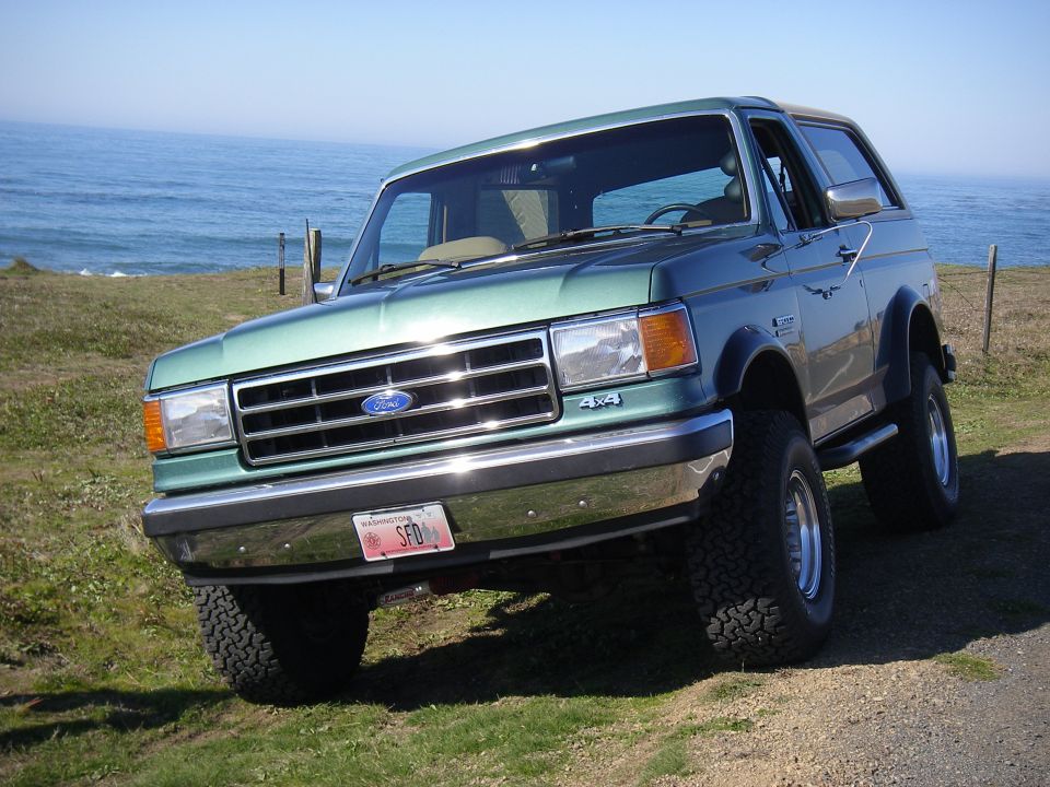 Green 1990 Ford Bronco parked on a grassy cliff overlooking the ocean