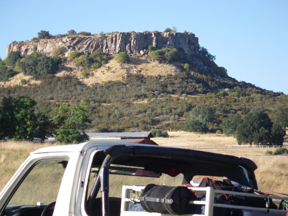 White Ford Bronco with black soft top and roll bar, parked in front of a rocky hill