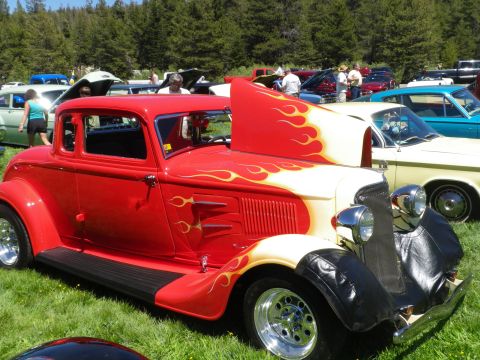 1991 Ford Bronco - A red hot rod coupe with flame decals is parked on grass at an outdoor car show with other vehicles.