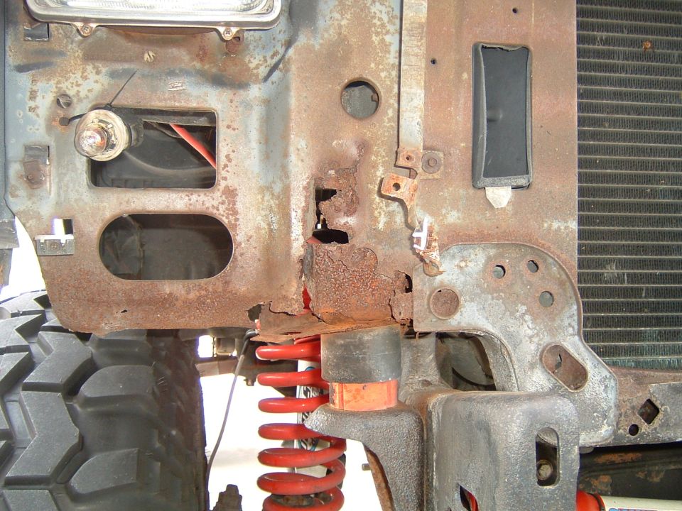 Rusted-through body mount and inner fender on a Bronco, with red coil spring and radiator visible