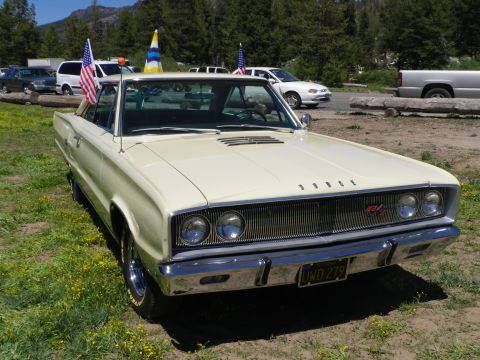 1991 Ford Bronco - A cream 1967 Dodge Coronet R/T coupe is parked on grass with American flags, with other vehicles in the background.