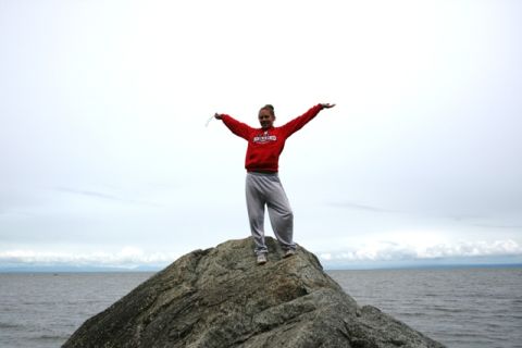 1990 Chevrolet Suburban - A person stands with arms outstretched atop a large rock formation near the water under an overcast sky.