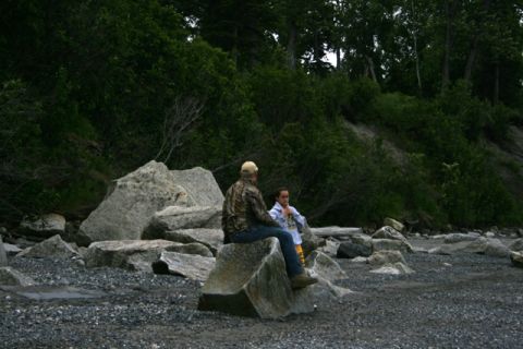 1990 Chevrolet Suburban - Two individuals rest on large boulders along a rocky coastline, with dense foliage forming the backdrop.