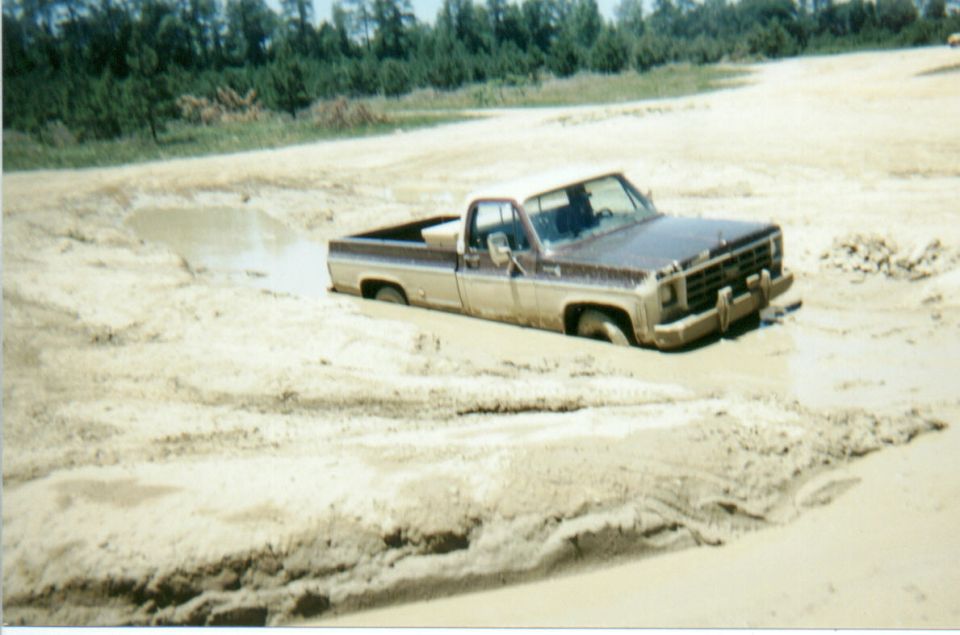 Two-tone brown Chevrolet squarebody pickup buried to its bumpers in a wet mud pit