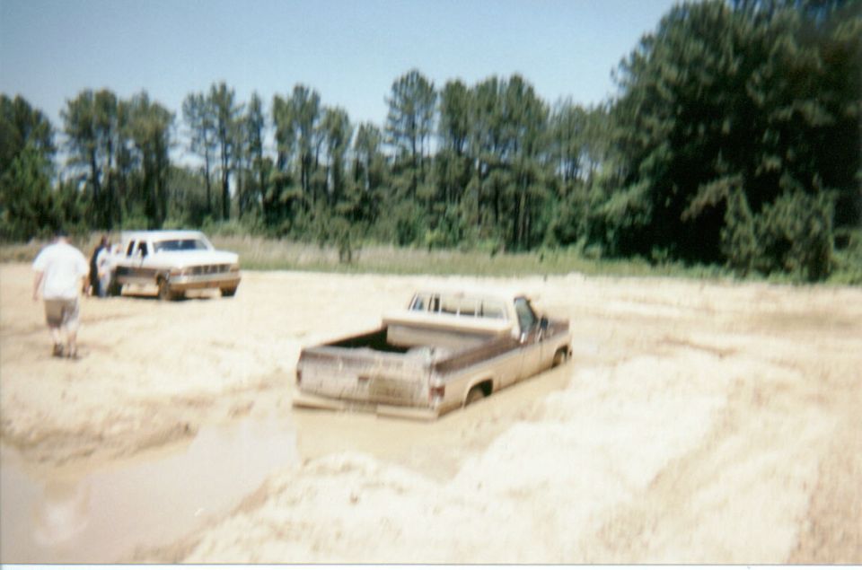 Square-body Chevrolet pickup stuck up to its doors in a muddy pit