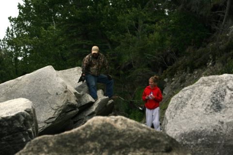 1990 Chevrolet Suburban - Two people explore a rocky area with dense trees in the background.