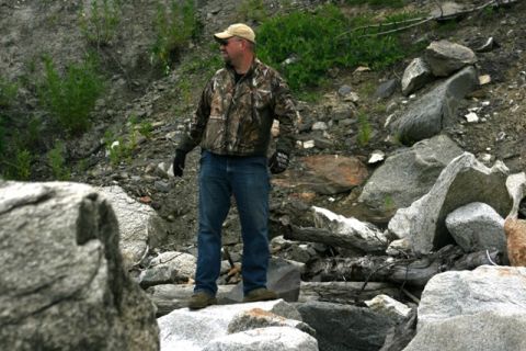 1990 Chevrolet Suburban - A man stands in a rocky outdoor environment, wearing a camouflage jacket and jeans.