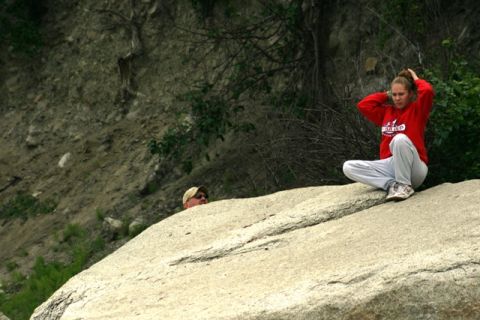 1990 Chevrolet Suburban - Two people are in a rocky outdoor area, with one person partially hidden behind a large boulder.