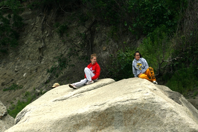 Two young women sitting on a large rock outdoors