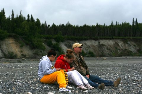 1990 Chevrolet Suburban - People relax on a pebble beach with a forested cliff face behind them.