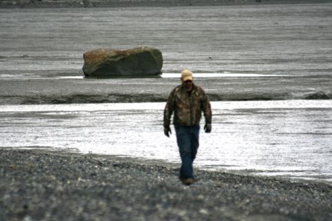 1990 Chevrolet Suburban - A man walks across a desolate, rocky landscape near a body of water.
