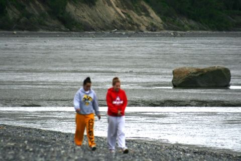 1990 Chevrolet Suburban - Two individuals stroll along a gravelly shoreline, with a prominent boulder resting in the wet, flat terrain behind them.