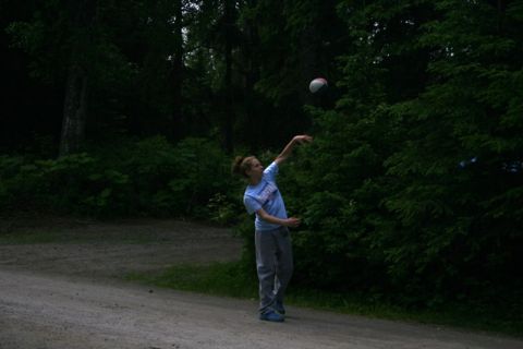 1990 Chevrolet Suburban - A person is captured mid-throw as they toss a ball in a park setting surrounded by trees.