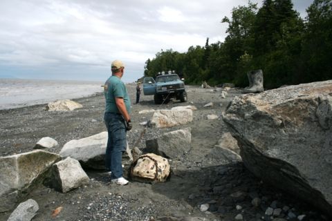 1990 Chevrolet Suburban - A light blue 1990 Chevrolet Suburban is parked on a rocky beach near the water, with a person standing nearby.