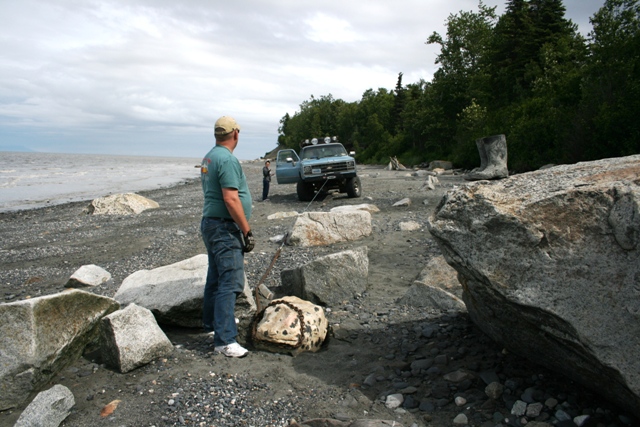 Light blue 1990 Chevrolet Suburban with off-road lights on roof, parked on a rocky beach