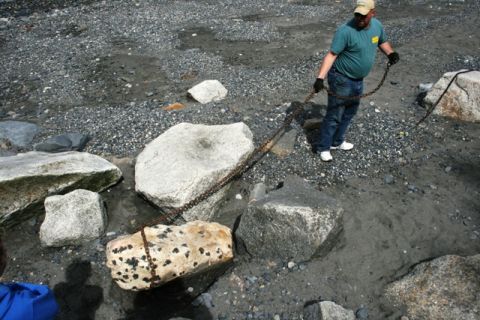 1990 Chevrolet Suburban - A man uses a chain to move a large rock on a beach with scattered boulders and gravel.