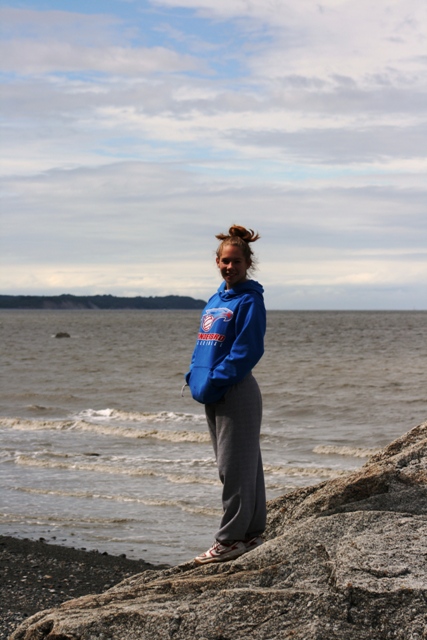1990 Chevrolet Suburban - A young woman stands on a rocky shoreline with the ocean and cloudy sky in the background.