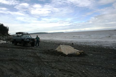 1990 Chevrolet Suburban - A person stands next to a green SUV parked on a rocky shore with the ocean in the background.
