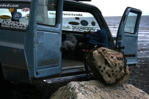 1990 Chevrolet Suburban - A blue van sits on a rocky shore with its doors open, facing the ocean.