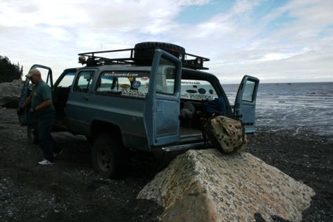 1990 Chevrolet Suburban - A blue SUV is parked on a rocky shore with the ocean in the background and a person standing by the driver's door.