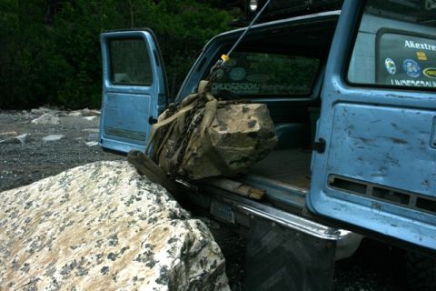1990 Chevrolet Suburban - Loading a large rock into a blue SUV using chains and straps at a rocky outdoor location.