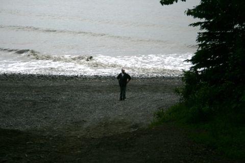 1990 Chevrolet Suburban - A lone figure stands on a pebble beach as waves crash ashore under an overcast sky.