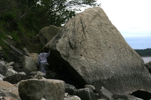 1990 Chevrolet Suburban - A person stands next to a huge boulder on a rocky shore, with trees and water in the background.