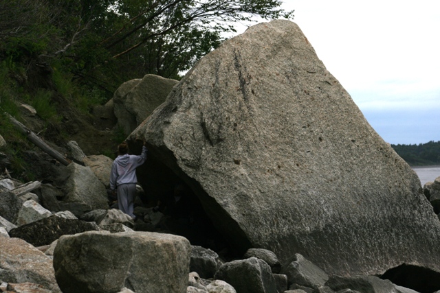 Person touches a massive boulder on a rocky coastline