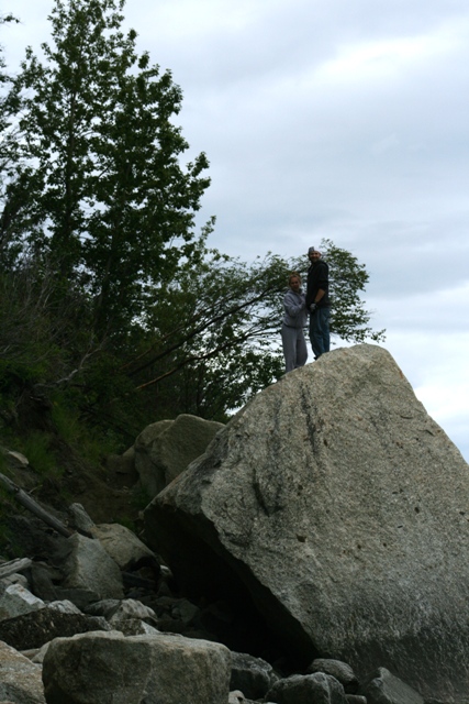 1990 Chevrolet Suburban - Two individuals are positioned atop a prominent rock, with a backdrop of trees and an overcast sky.