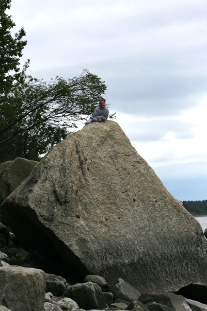 1990 Chevrolet Suburban - A person sits on a large rock formation overlooking a body of water under a cloudy sky.