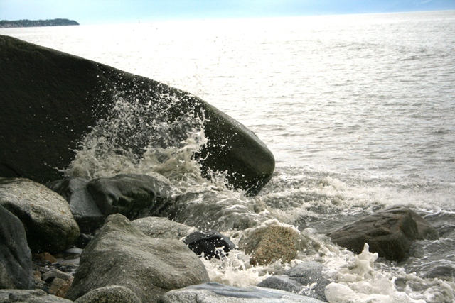 Waves crash against dark rocks on a bright, sunny day