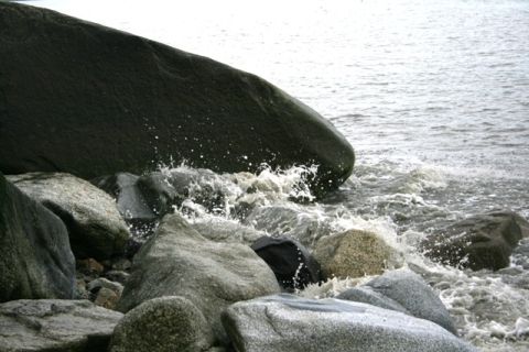 1990 Chevrolet Suburban - Water splashes against large rocks on a shoreline.