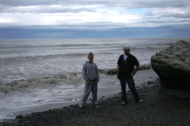 Two people stand on a rocky beach with waves crashing