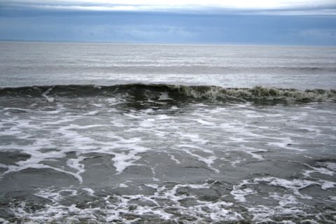 1990 Chevrolet Suburban - The ocean churns with white foam under a gray sky.
