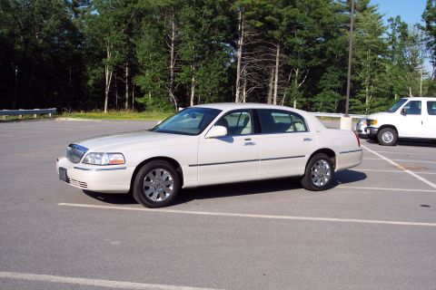 2001 Ford Crown Victoria - A white Lincoln Town Car is parked in a lot next to a white van.