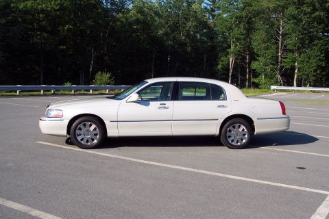 2001 Ford Crown Victoria - A white Lincoln Town Car is parked in an empty lot with trees in the background.