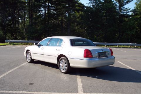 2001 Ford Crown Victoria - Rear view of a white sedan parked in an empty lot with trees in the background.