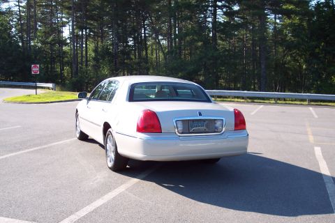 2001 Ford Crown Victoria - White Lincoln Town Car parked in a lot, seen from the rear. Trees and a stop sign are visible in the background.
