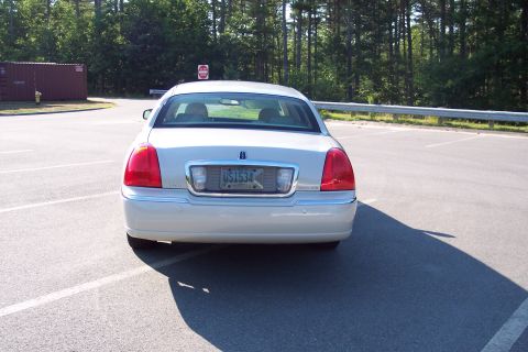 2001 Ford Crown Victoria - The rear of a beige Lincoln Town Car is shown parked in an empty lot with trees in the background.