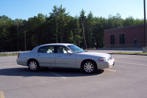 2001 Ford Crown Victoria - This Lincoln Town Car is parked in a lot with trees and a brick building behind it.