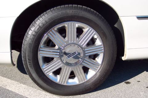 2001 Ford Crown Victoria - Close-up of a white Lincoln Town Car's wheel, chrome spokes and the Lincoln emblem.