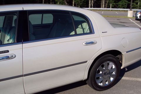 2001 Ford Crown Victoria - The side profile of a white sedan reveals its rear passenger door and wheel assembly.