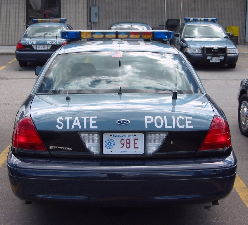 Rear view of a 1998 Ford Crown Victoria police car with 'STATE POLICE' on the trunk. Two other similar cars are parked behind it