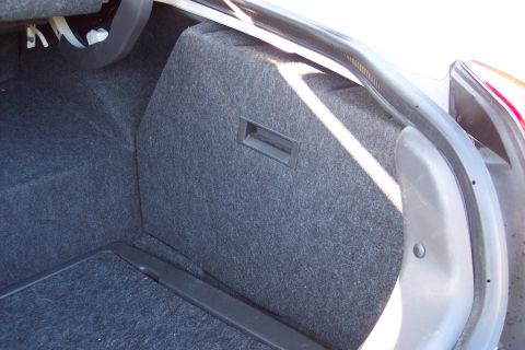 2001 Ford Crown Victoria - Open trunk of a white sedan with gray carpeting, showing a carpeted vertical partition panel with a recessed pull handle built against the…
