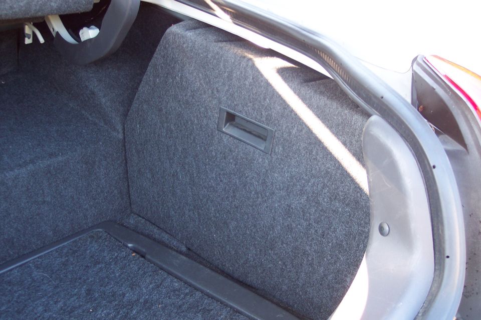 Carpeted trunk of a white sedan with a vertical divider panel and pull handle