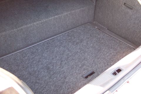 2001 Ford Crown Victoria - Interior view of an open trunk lined with gray carpet, showing the trunk floor, side walls, and a molded latch/handle recess near the trunk…